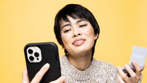 Asian woman looking at cell phone while holding an open refillable makeup compact during a virtual consultation with makeup artist to make sustainable swaps in her everyday beauty routine