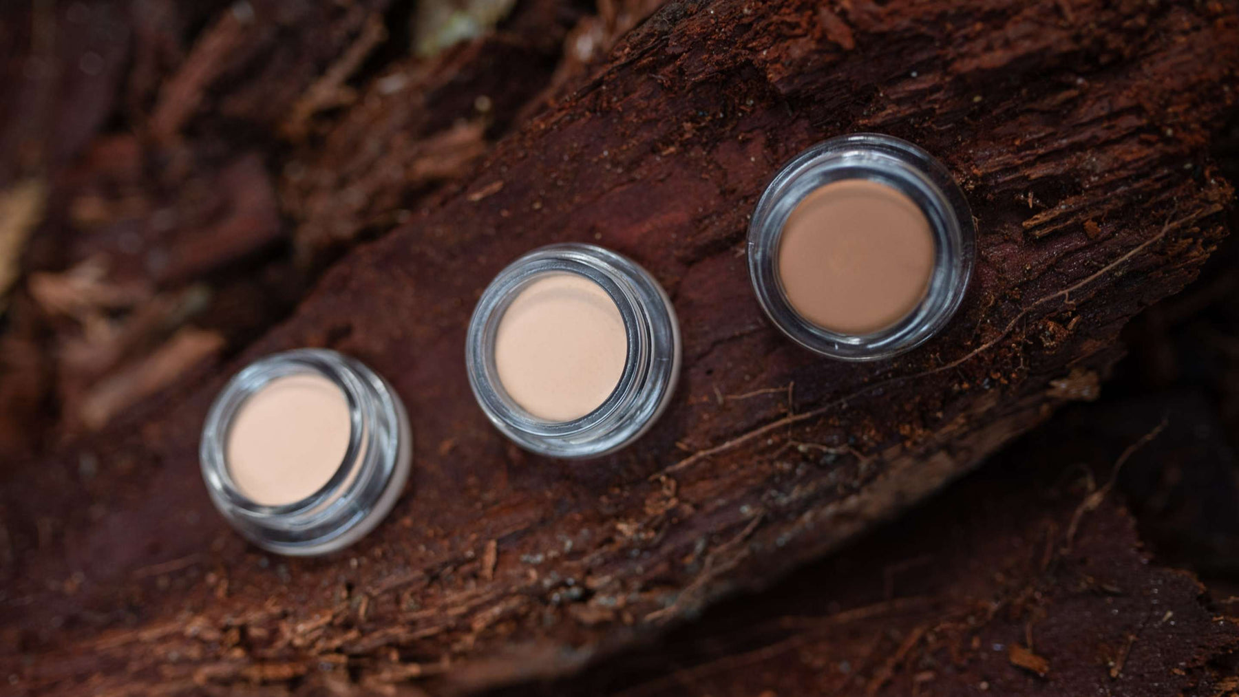 Three organic cream concealer pots open in a BC forest on Douglas Fir wood